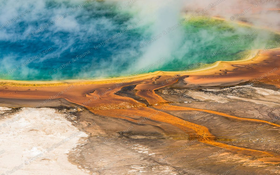 Aerial view of a blue hot spring rimmed with bands of orange, seen through drifting steam.
